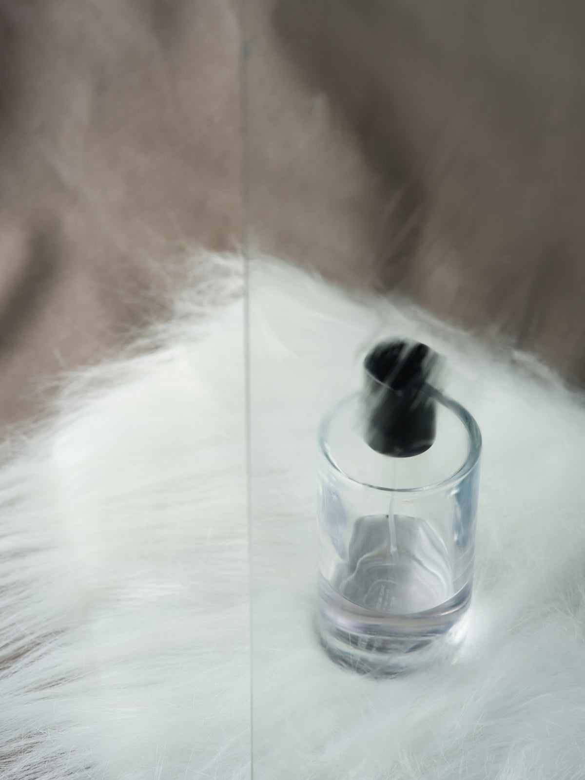 Clear perfume bottle with black cap on white fur
